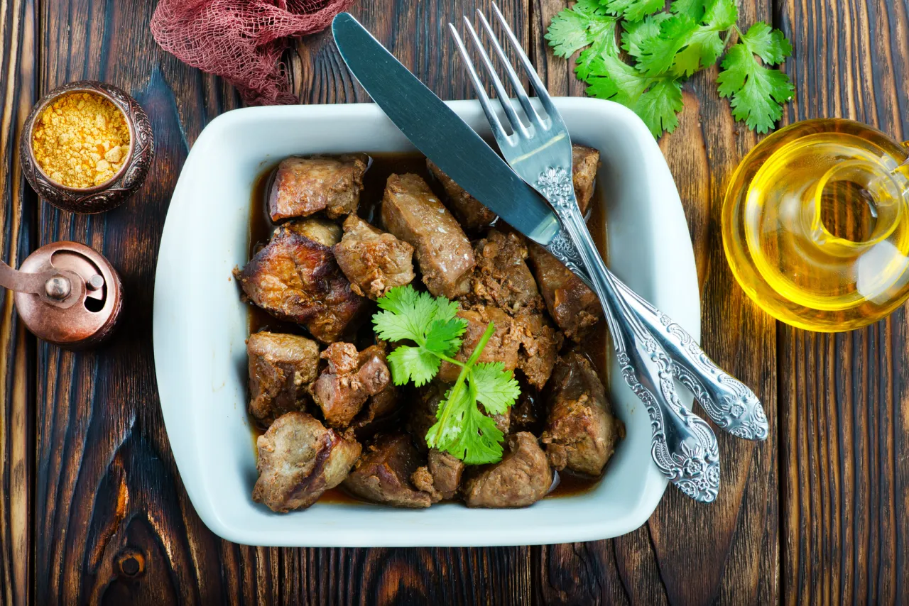 Duszona wątróbka w sosie, z gałązką kolendry. Czy wątróbka jest lekkostrawna? Zależy od sposobu przygotowania.