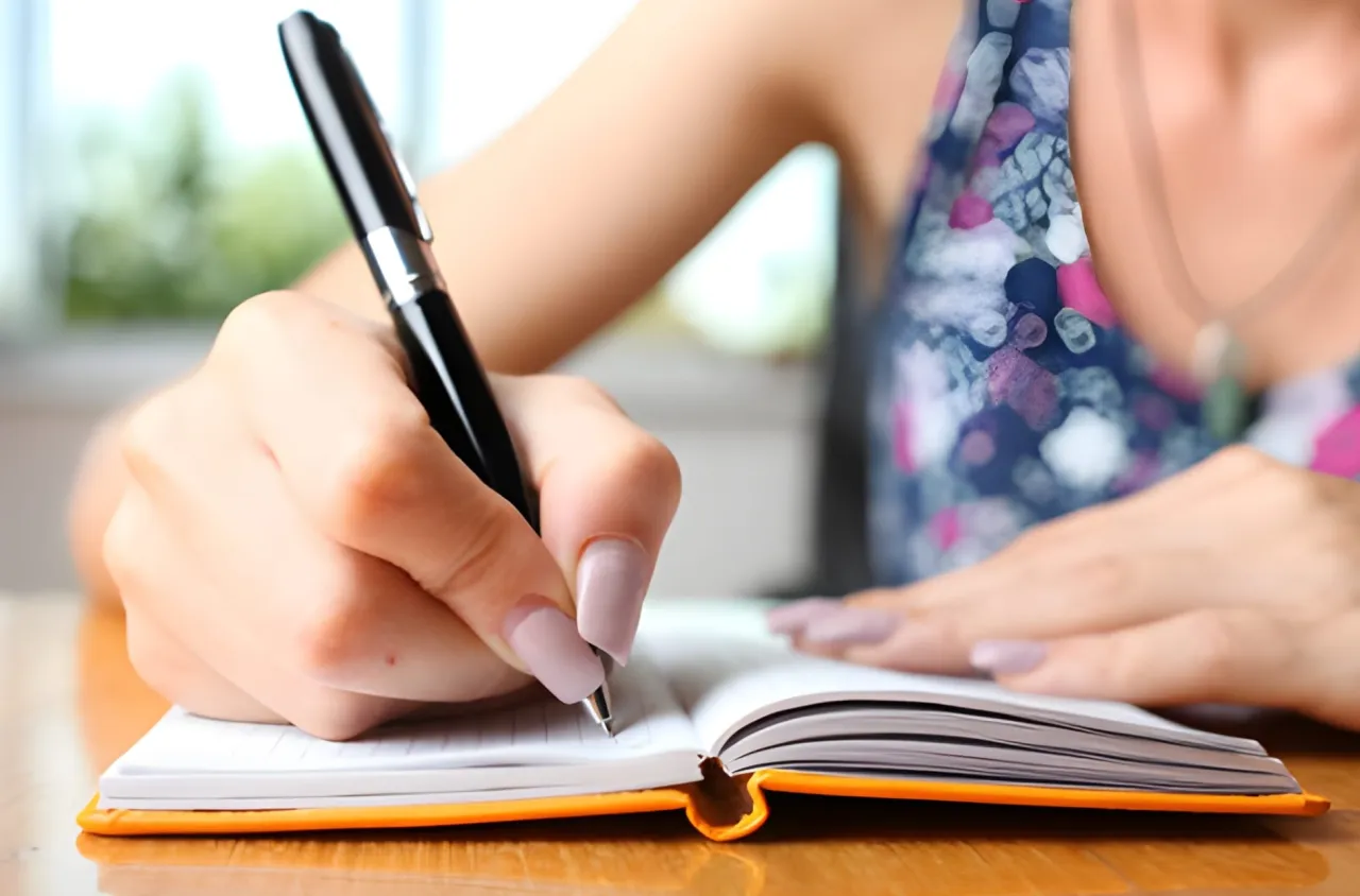 Dłoń z długopisem pisze w notatniku, zaczynając swoją historię. To pierwszy krok, jak napisać książkę.