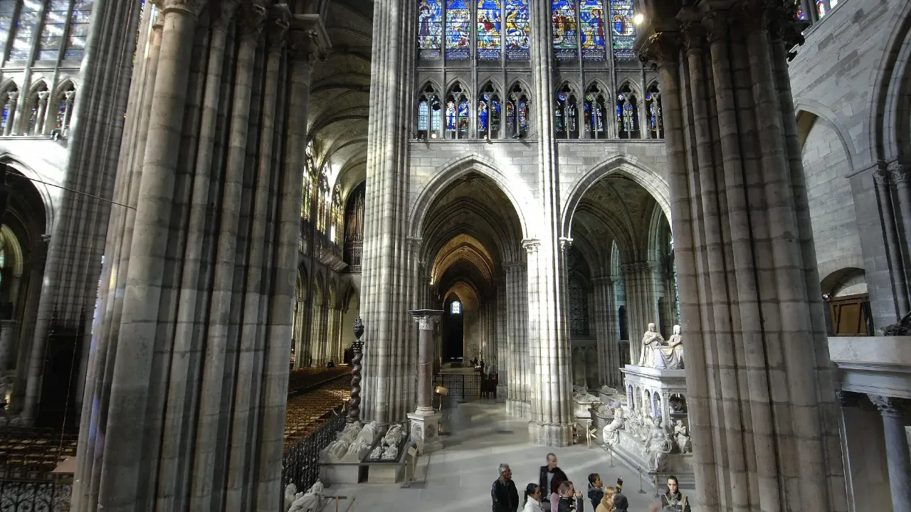 Wnętrze bazyliki Saint-Denis z imponującymi kolumnami, witrażami i nagrobkami.