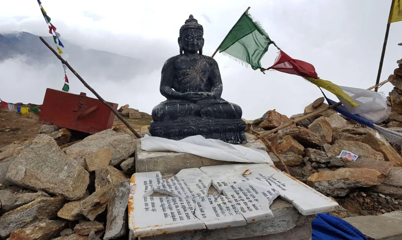 Posąg Buddy na szczycie góry, gdzie dominuje buddyzm. Wokół modlitewne chorągiewki i kamienie.