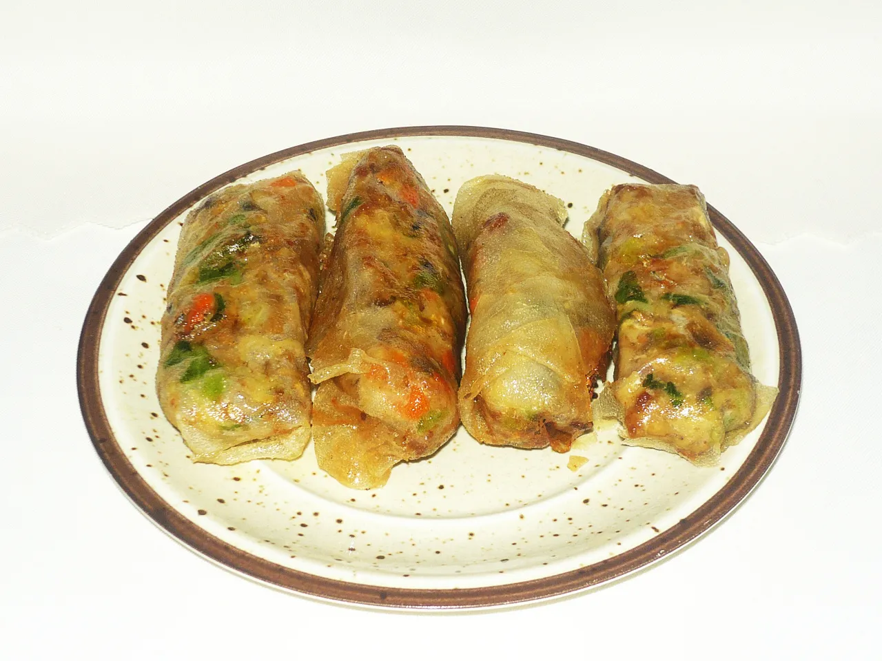 Cztery złociste sajgonki z mięsem mielonym i warzywami, ułożone na talerzu w groszki.