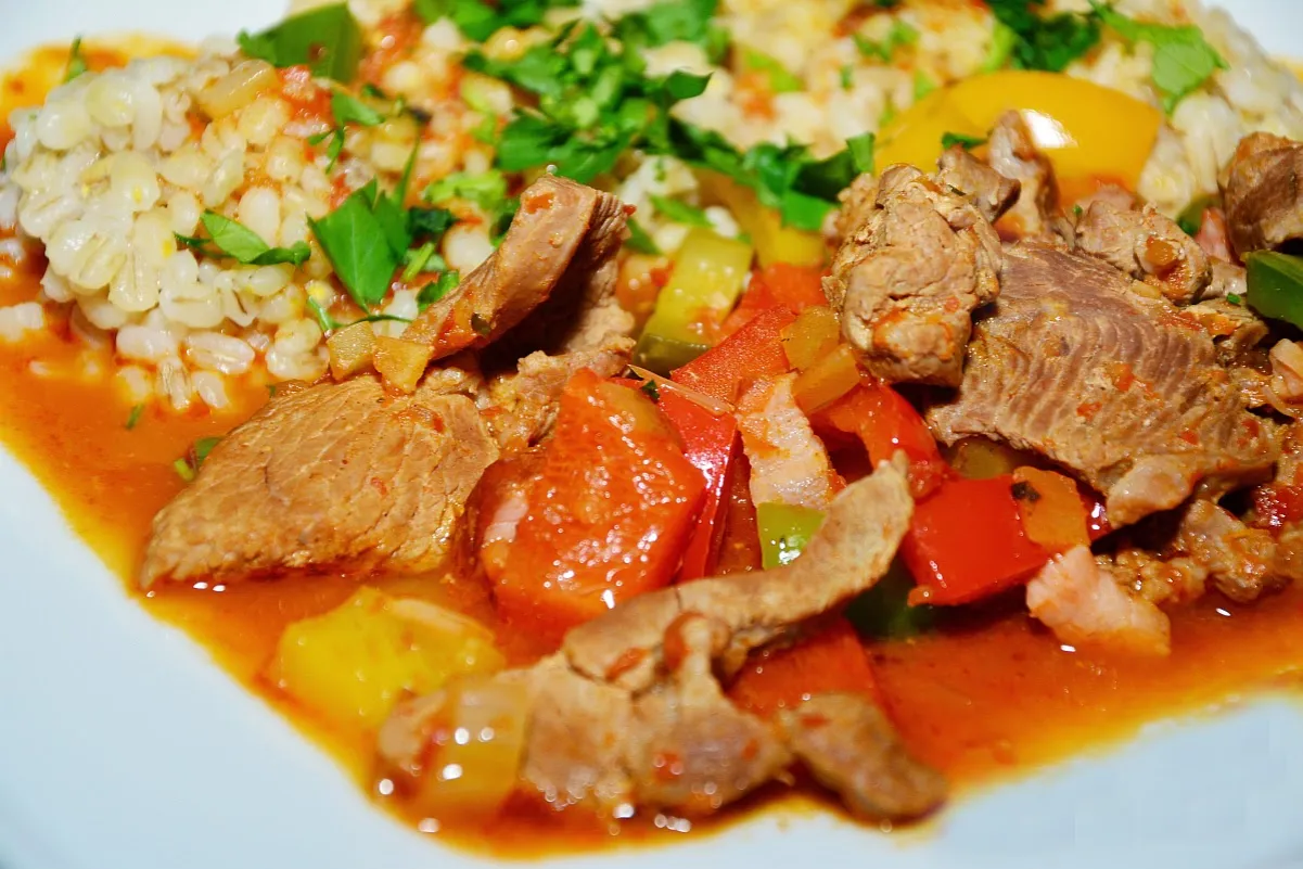 Mięso na gulasz, kawałki wołowiny duszone z papryką i pomidorami, podane z kaszą jęczmienną i posypane natką pietruszki.