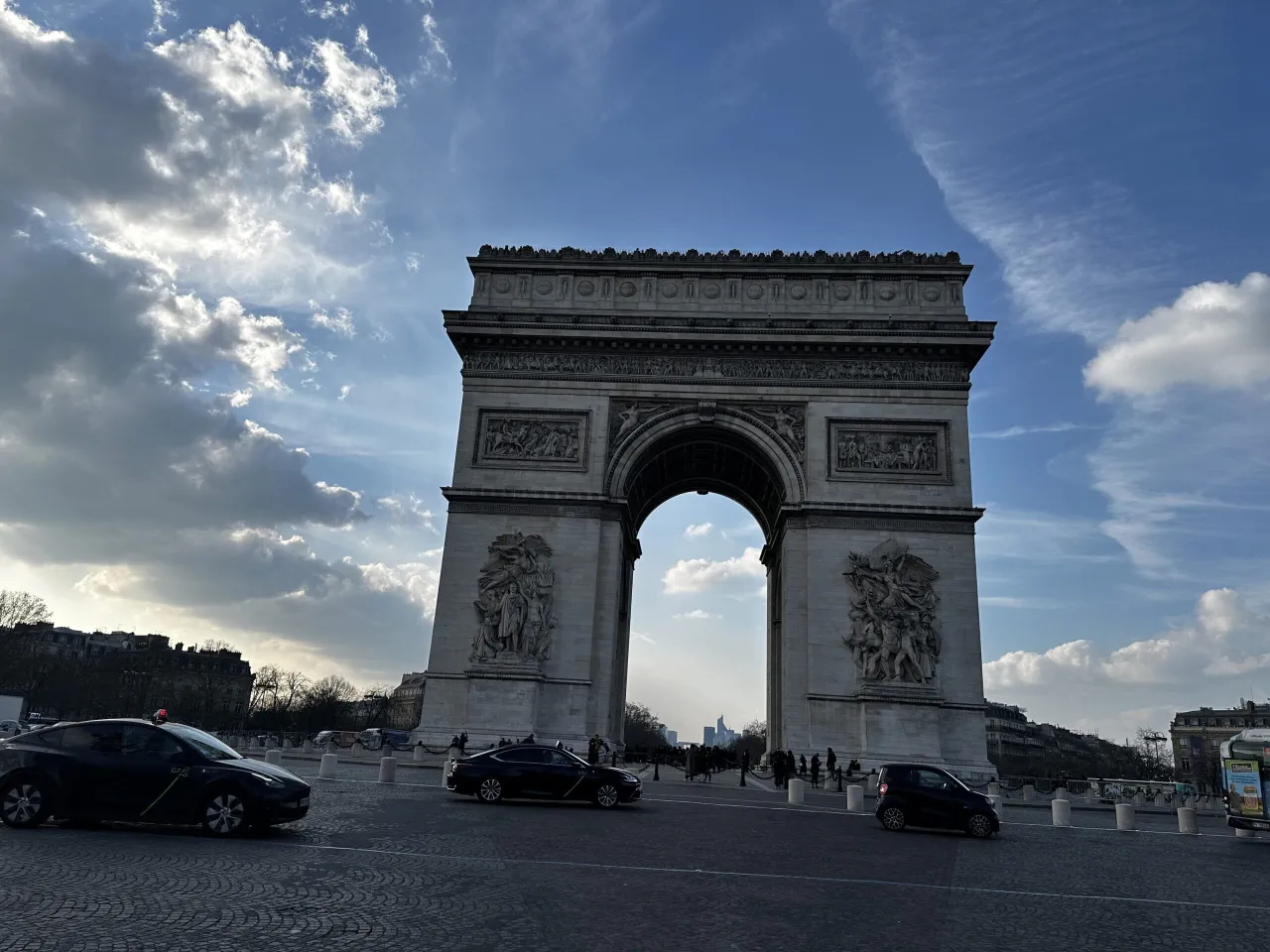 Łuk Triumfalny w 8 dzielnicy Paryża, z samochodami na brukowanej drodze i chmurami na niebie.