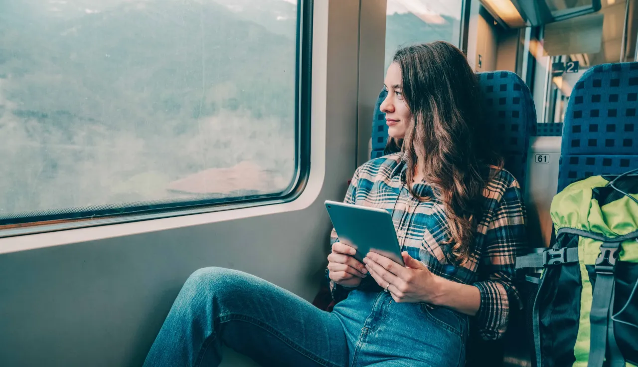 Kobieta w pociągu z tabletem szuka inspiracji, jak szukać tanich nocleg&oacute;w za granicą.