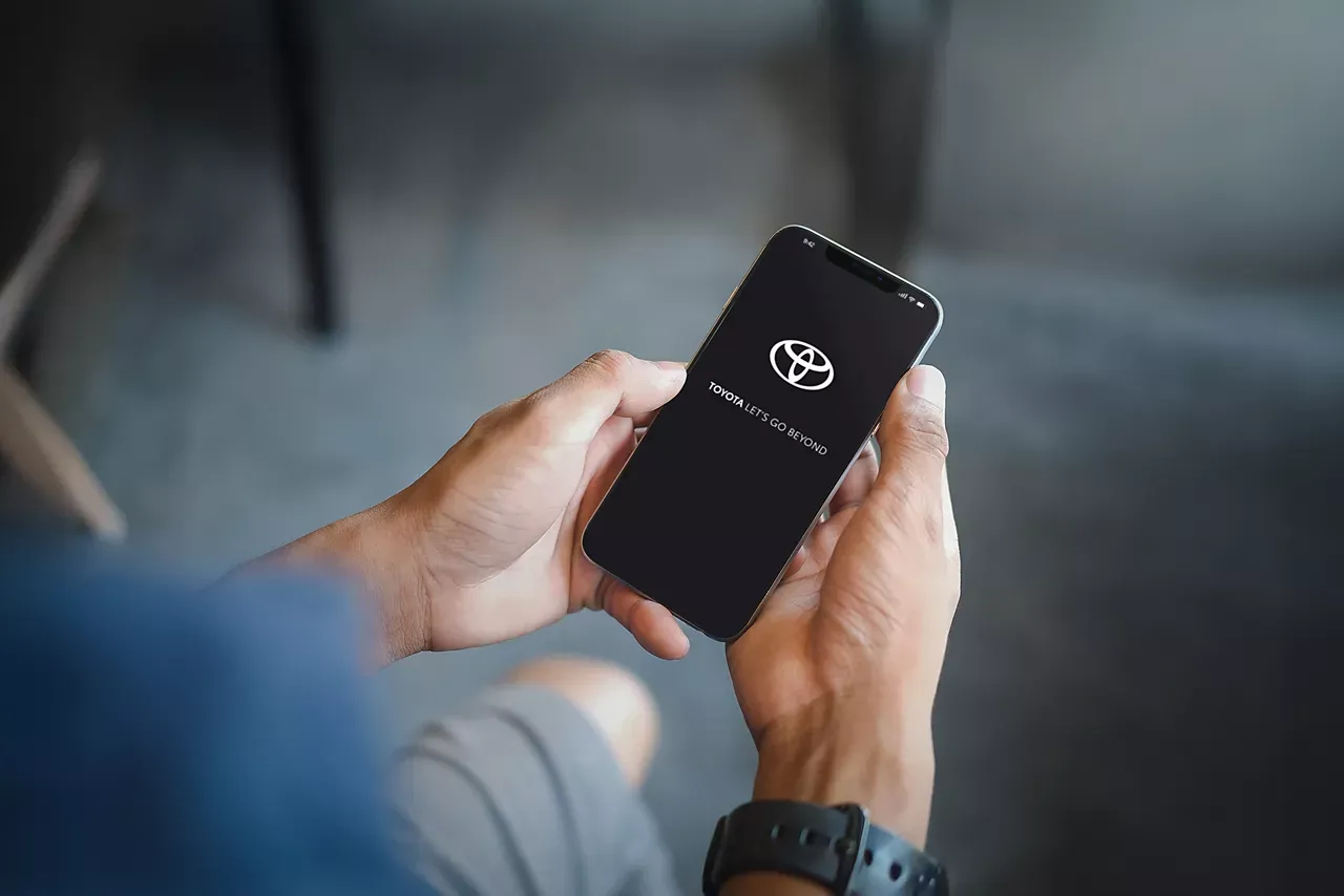 Dłonie trzymają smartfon z logo Toyoty. Aplikacja pokazuje, jak działa bluetooth low energy Toyota, łącząc się z samochodem.