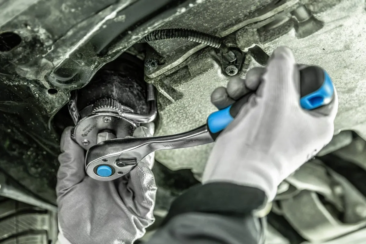 mechanik wymieniający olej w samochodzie, miska olejowa, klucz do filtra oleju