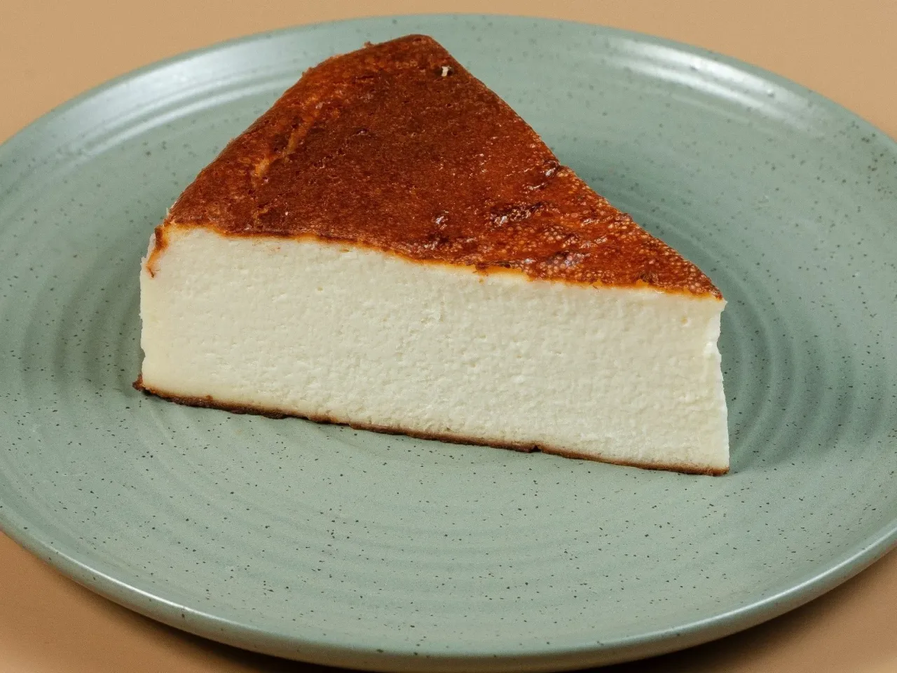 Pyszny kawałek sernika pieczonego bez spodu, z lekko przypieczoną górą, na zielonym talerzu.