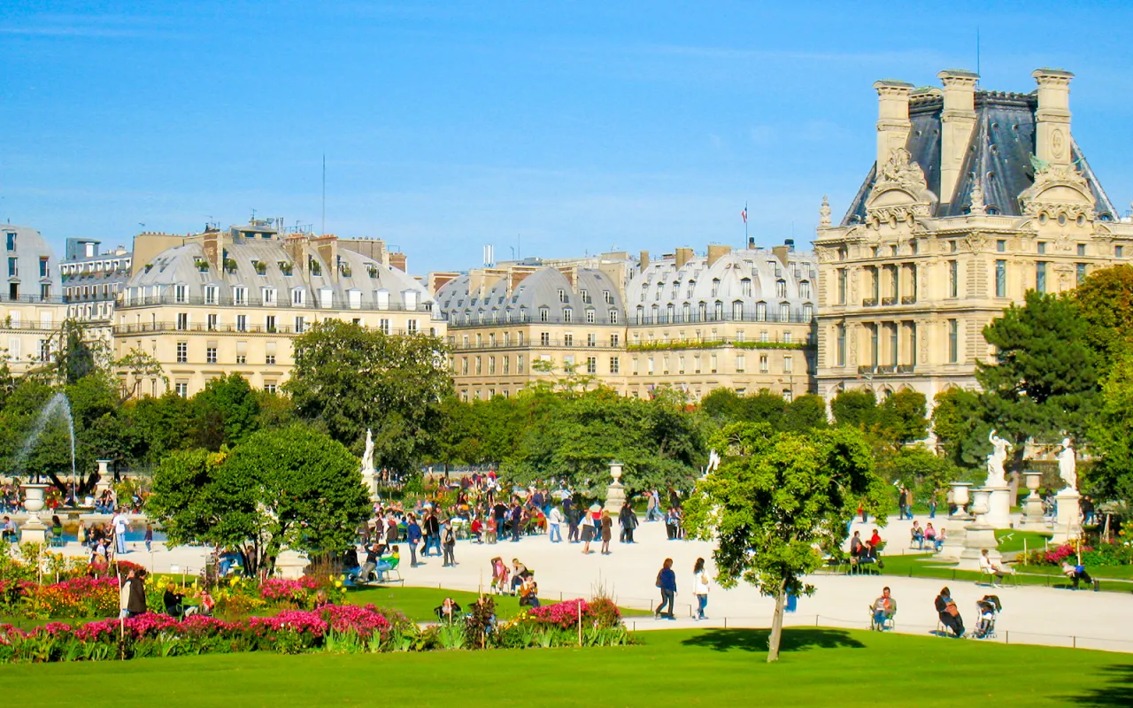 Spacerowicze w 1 dzielnicy Paryża, w Ogrodach Tuileries, podziwiają architekturę i kwitnące kwiaty.