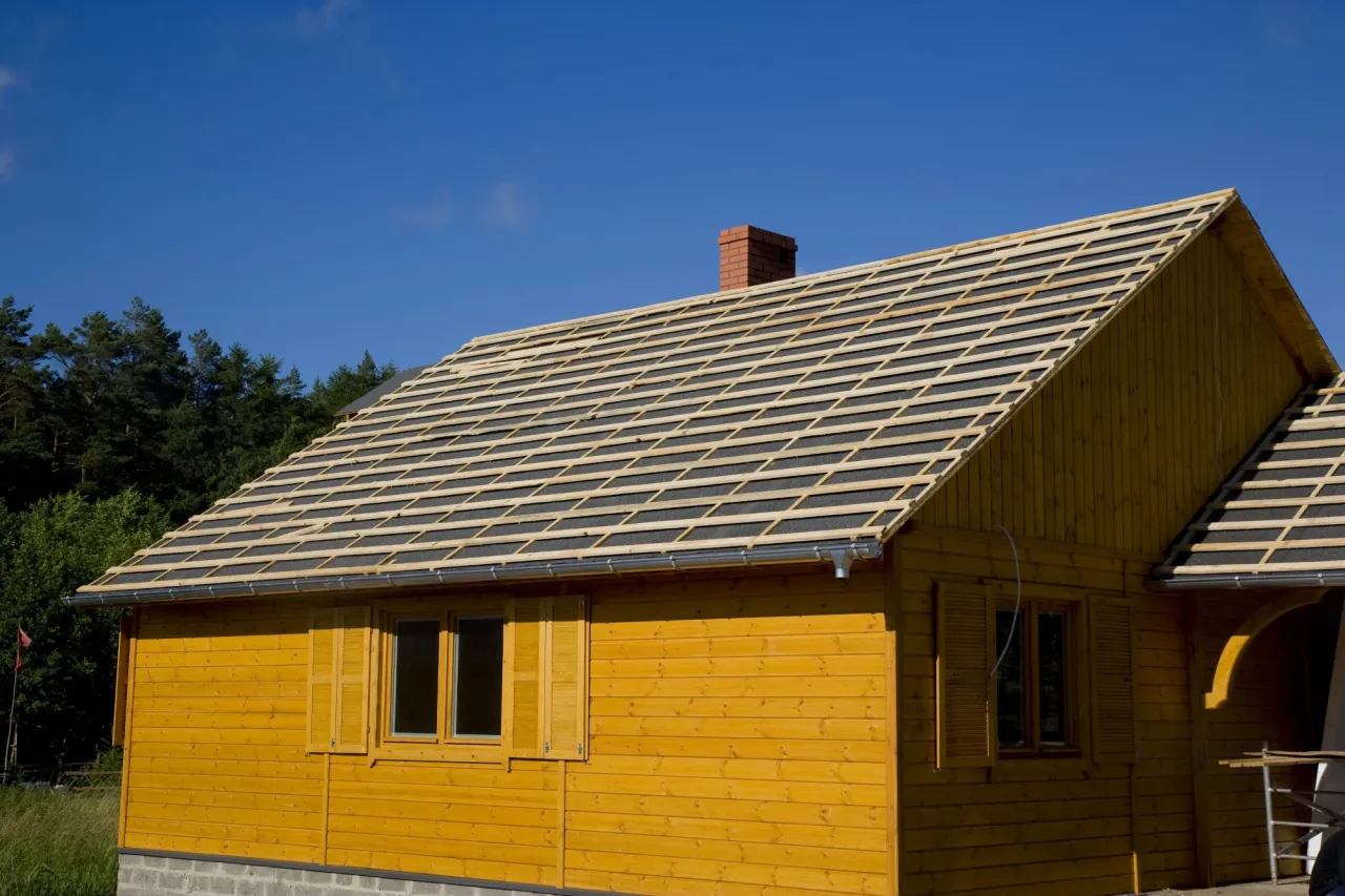 Drewniany dom w trakcie budowy, z widocznym rusztem na dachu, gotowym pod montaż blachodachówki.