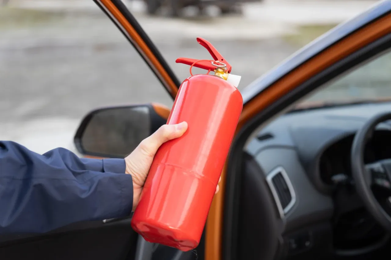 Kierowca szukający gaśnicy w bagażniku pod rzeczami