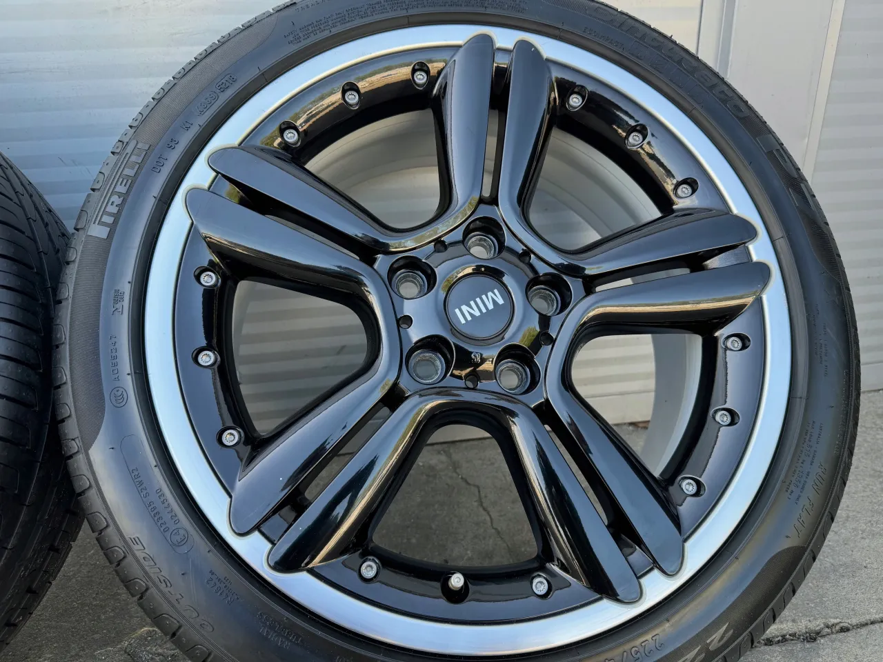 Błyszczące, czarne felgi Mini Cooper z pięcioma ramionami i srebrną obręczą. Koło zapasowe w Mini Cooper zazwyczaj znajduje się pod podłogą bagażnika.