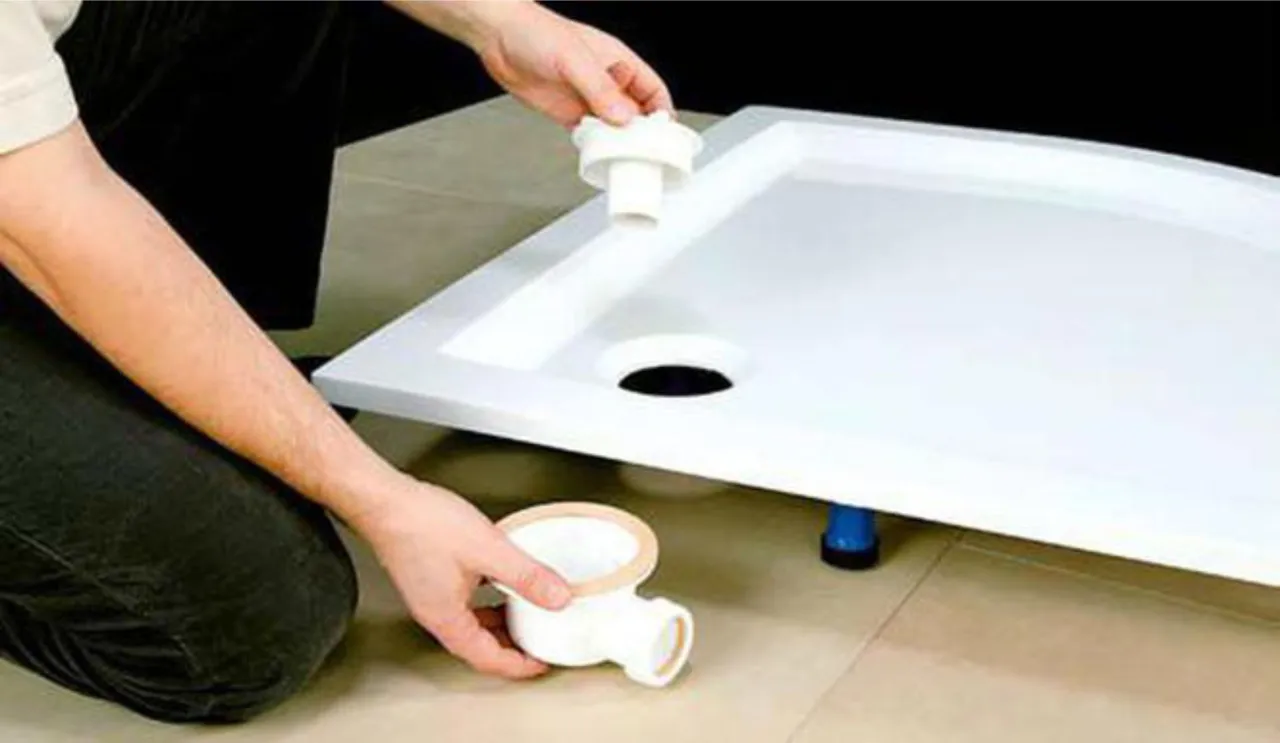 Montaż brodzika wysokiego: ręka trzyma element syfonu, przygotowując go do połączenia z odpływem brodzika.