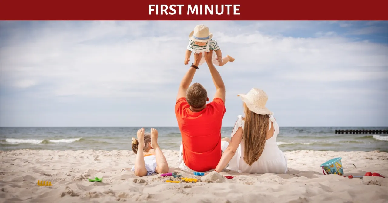 Rodzinne wakacje z dzieckiem nad morzem. Ojciec podrzuca niemowlę na plaży, podczas gdy matka i starsze dziecko odpoczywają.