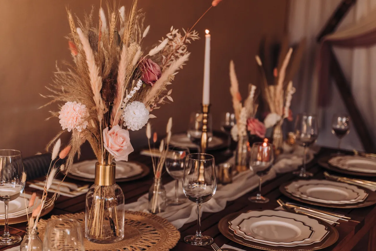 Elegancka dekoracja sali weselnej w stylu boho: bukiet z traw pampasowych, róż i świec. Inspiracje na przyjęcie.