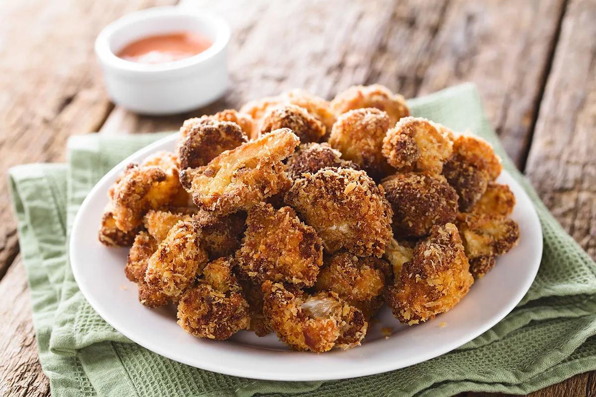 Chrupiące różyczki kalafiora w panko, podane na białym talerzu, z sosem w tle. Idealna przekąska!