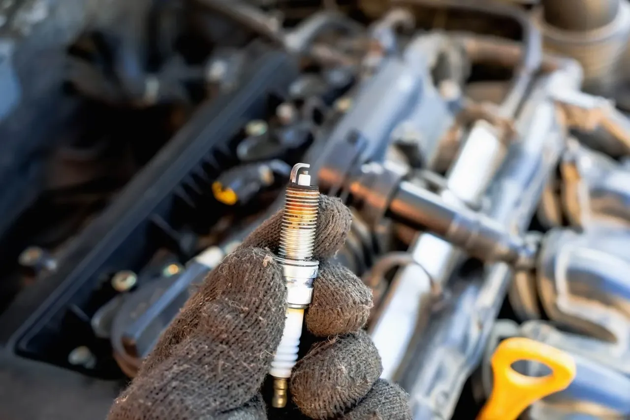 Ręka w rękawicy trzyma świecę zapłonową, gotową do wymiany. To jeden z objawów problemów z silnikiem.