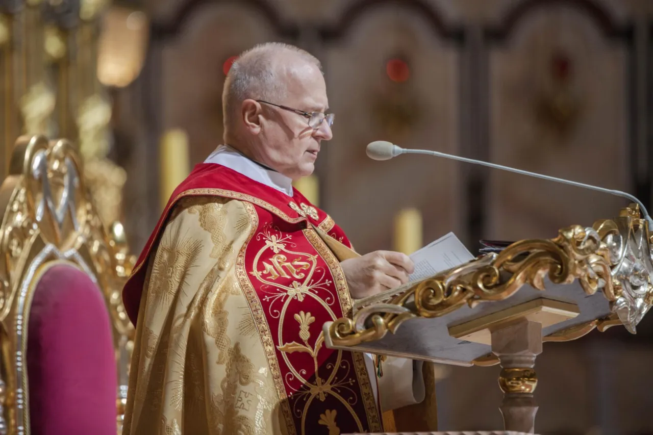Ksiądz w bogato zdobionej szacie celebruje nieszpory za zmarłego, czytając z księgi przy ozdobnym pulpicie.