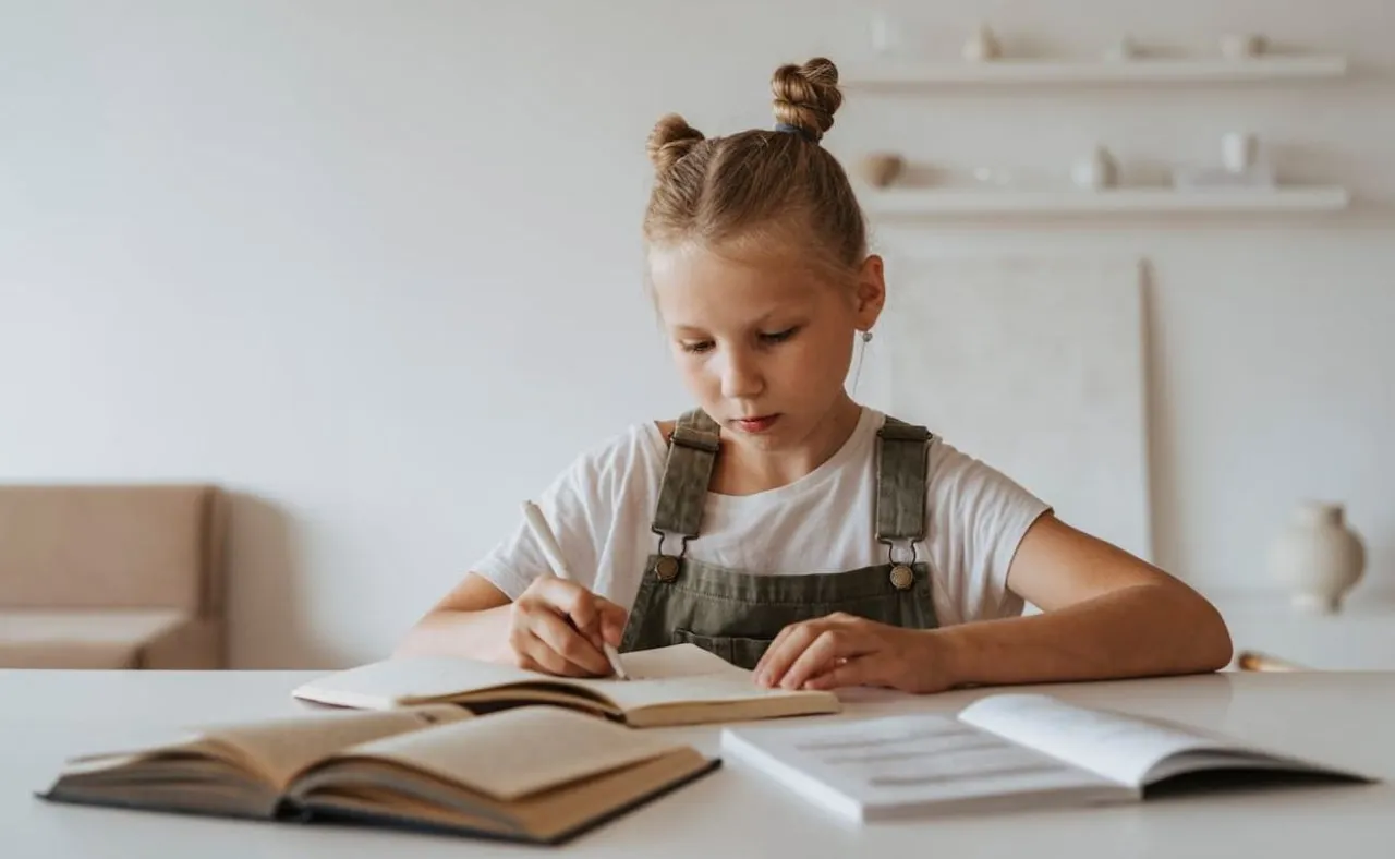 Dziewczynka z kitkami uczy się w domu, pisząc w zeszycie. To może być początek drogi, jak przejść na nauczanie domowe.