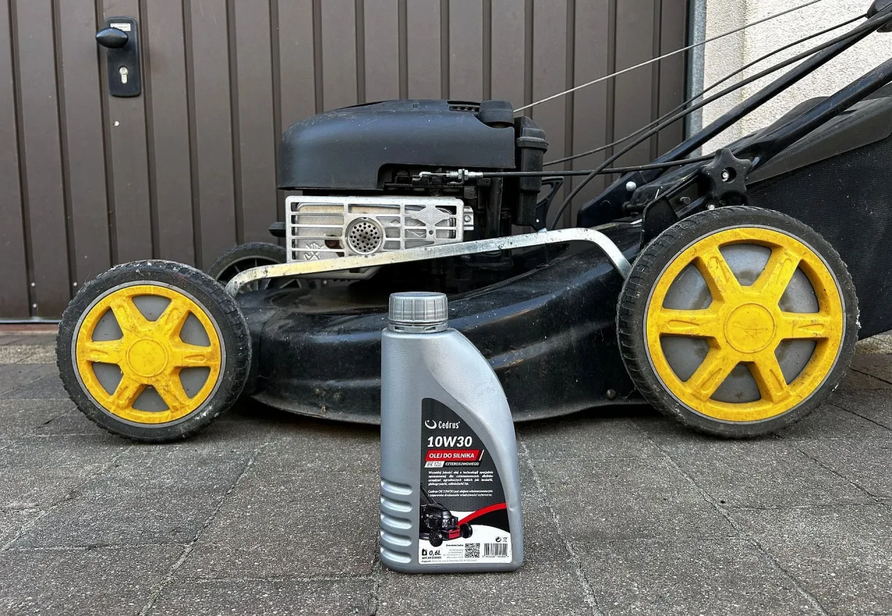 Butelka oleju Cedrus 10W30 do kosiarki czterosuwowej stoi przed kosiarką.