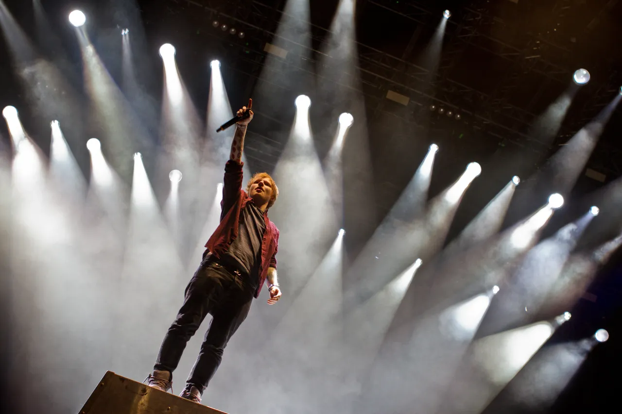 Ed Sheeran na scenie, w świetle reflektor&oacute;w, śpiewa dla tłumu. Ciekawe, ile zarabia Ed Sheeran za takie występy!