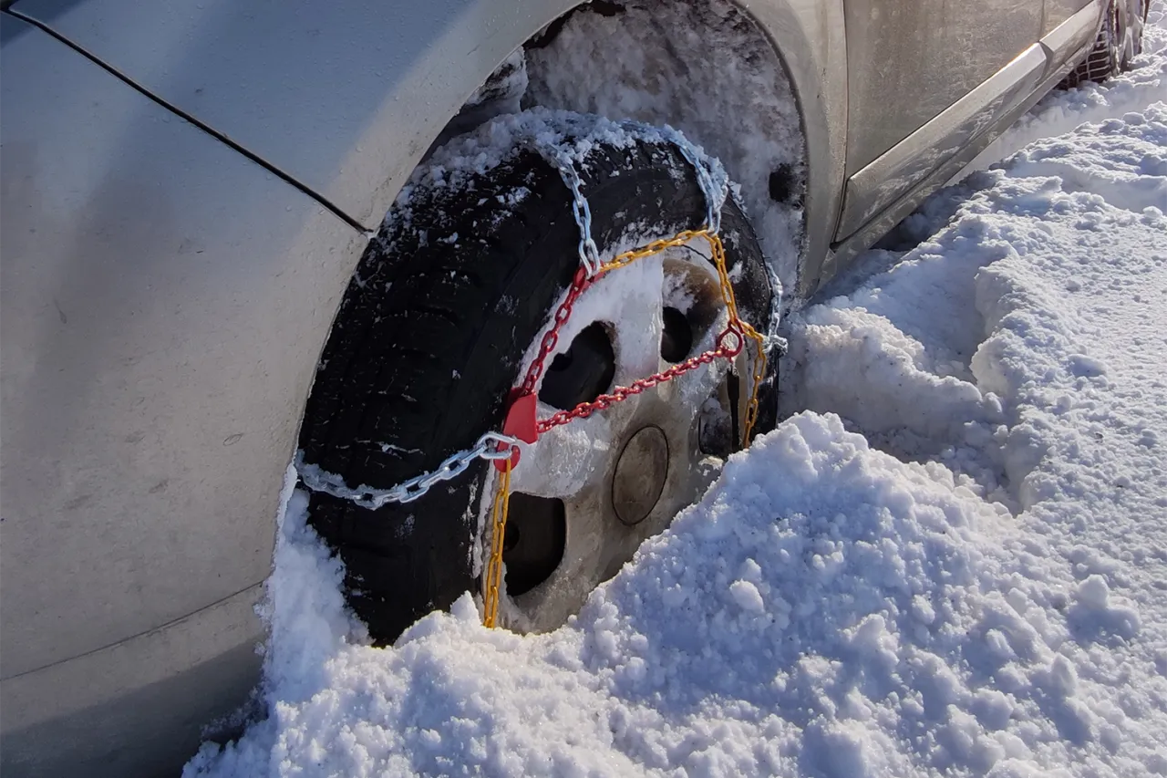 Samoch&oacute;d w zaspie, na kole założone łańcuchy. Uniknij mandatu za brak łańcuch&oacute;w w Polsce, pamiętaj o zimowym wyposażeniu!