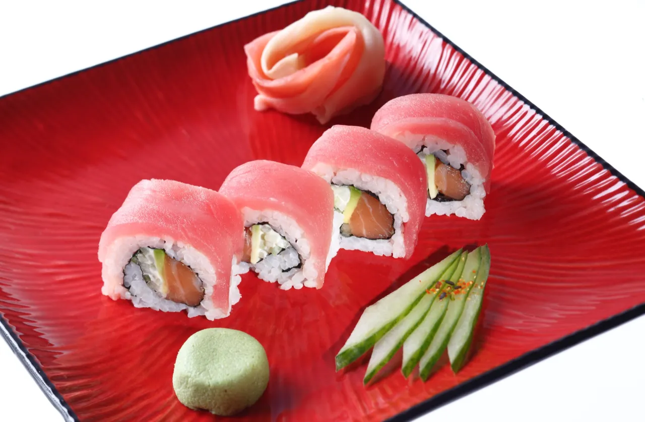 Roladki sushi z łososiem i awokado na czerwonym talerzu. Obok wasabi, marynowany imbir i plasterki og&oacute;rka. Idealne na letnie dni, gdy zastanawiasz się, jaka sałata do sushi będzie najlepsza.