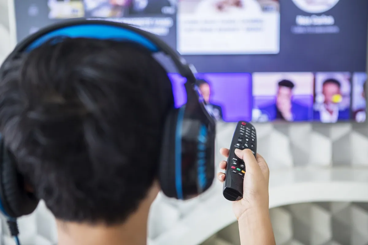 Osoba w słuchawkach z pilotem w ręku, szuka sposobu, jak podłączyć słuchawki bezprzewodowe do telewizora bez bluetooth.