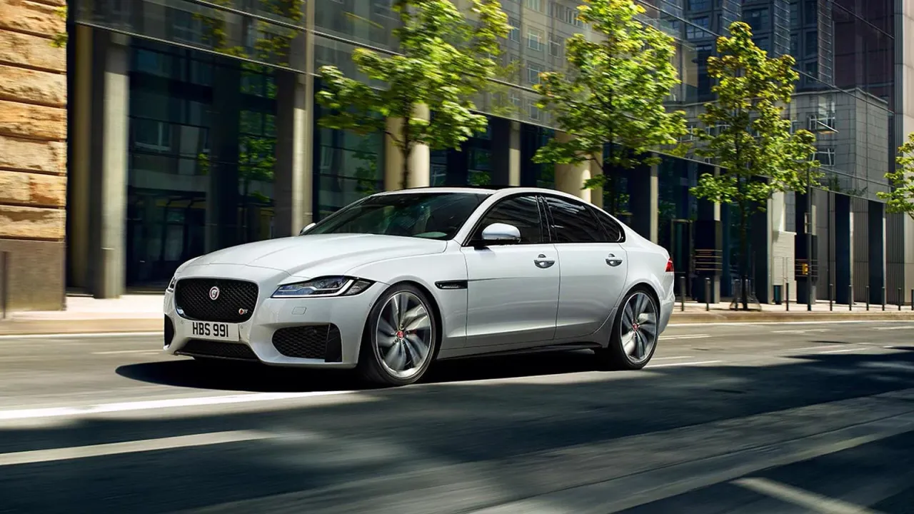 Biały Jaguar XF sunie po miejskiej ulicy. Czy jaguar xf jest drogi w utrzymaniu? To pytanie zadaje sobie wielu kierowców.