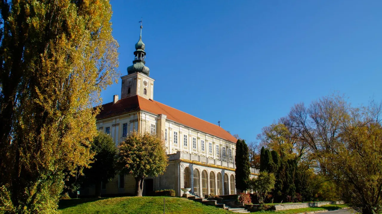 Pałac w Oławie, z wieżą i pomarańczowym dachem, otoczony jesienną zielenią. Idealne miejsce, co zobaczyć w Oławie.