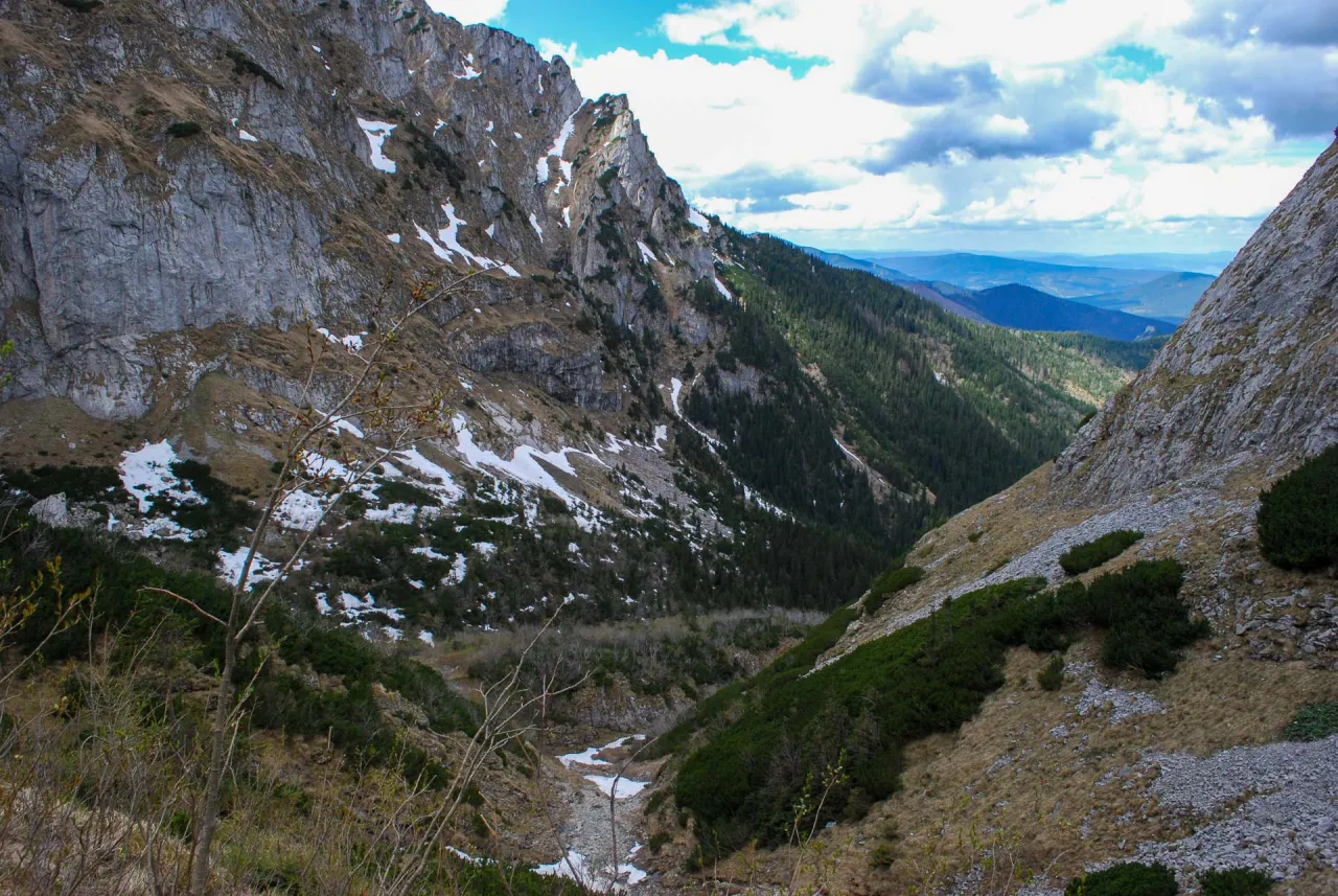 Majestatyczne góry z resztkami śniegu, skaliste zbocza i zielone lasy tworzą malowniczą dolinę małej łąki.