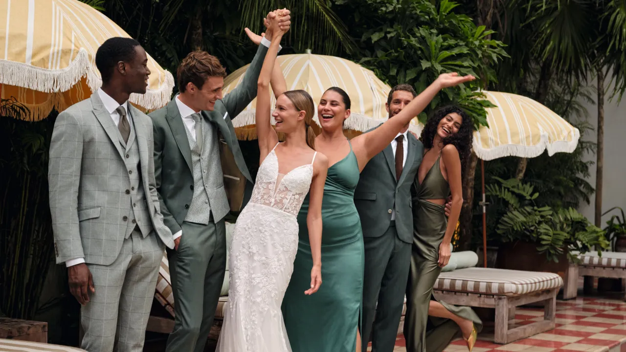 Grupa ludzi w eleganckim stroju formalnym świętuje na tle tropikalnej roślinności i ż&oacute;łtych parasoli.