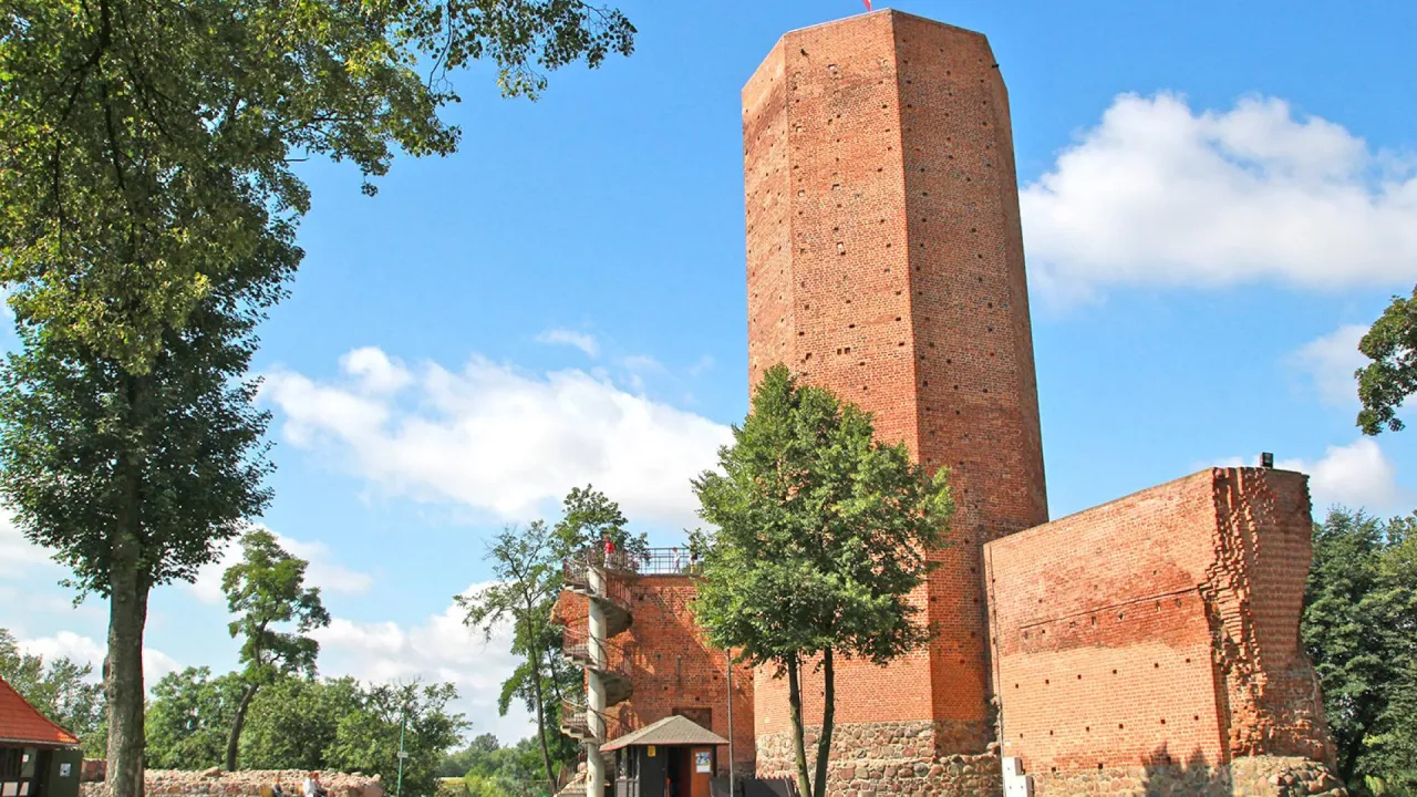 Ceglana wieża, część ruin zamku, przypomina o legendzie o mysiej wieży. Wok&oacute;ł drzewa i błękitne niebo.