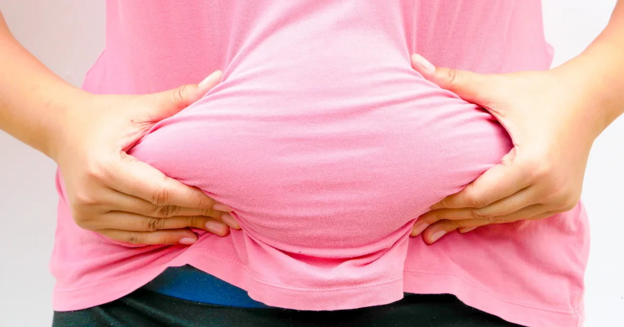 Dłonie ściskają brzuch w różowej koszulce, szukając odpowiedzi, jak pozbyć się brzucha po ciąży.