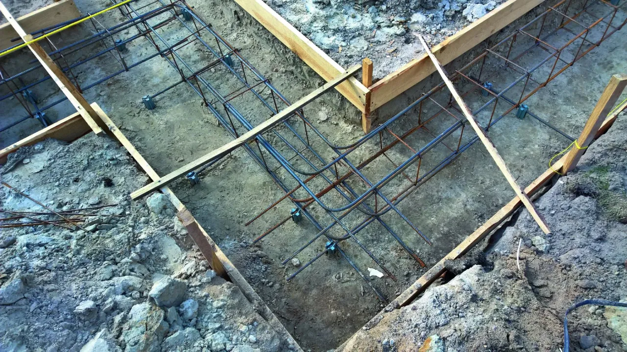 Siatka z prętów na zbrojenie fundamentów, gotowa do zalania betonem. Widać drewniane szalunki i podkładki dystansowe.