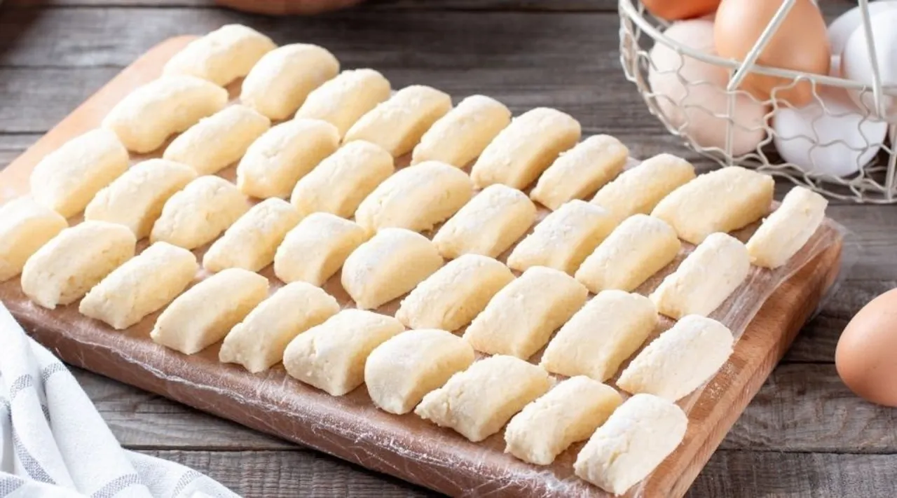 Gotowe do gotowania pierogi leniwe ułożone na desce. W tle koszyk z jajkami.