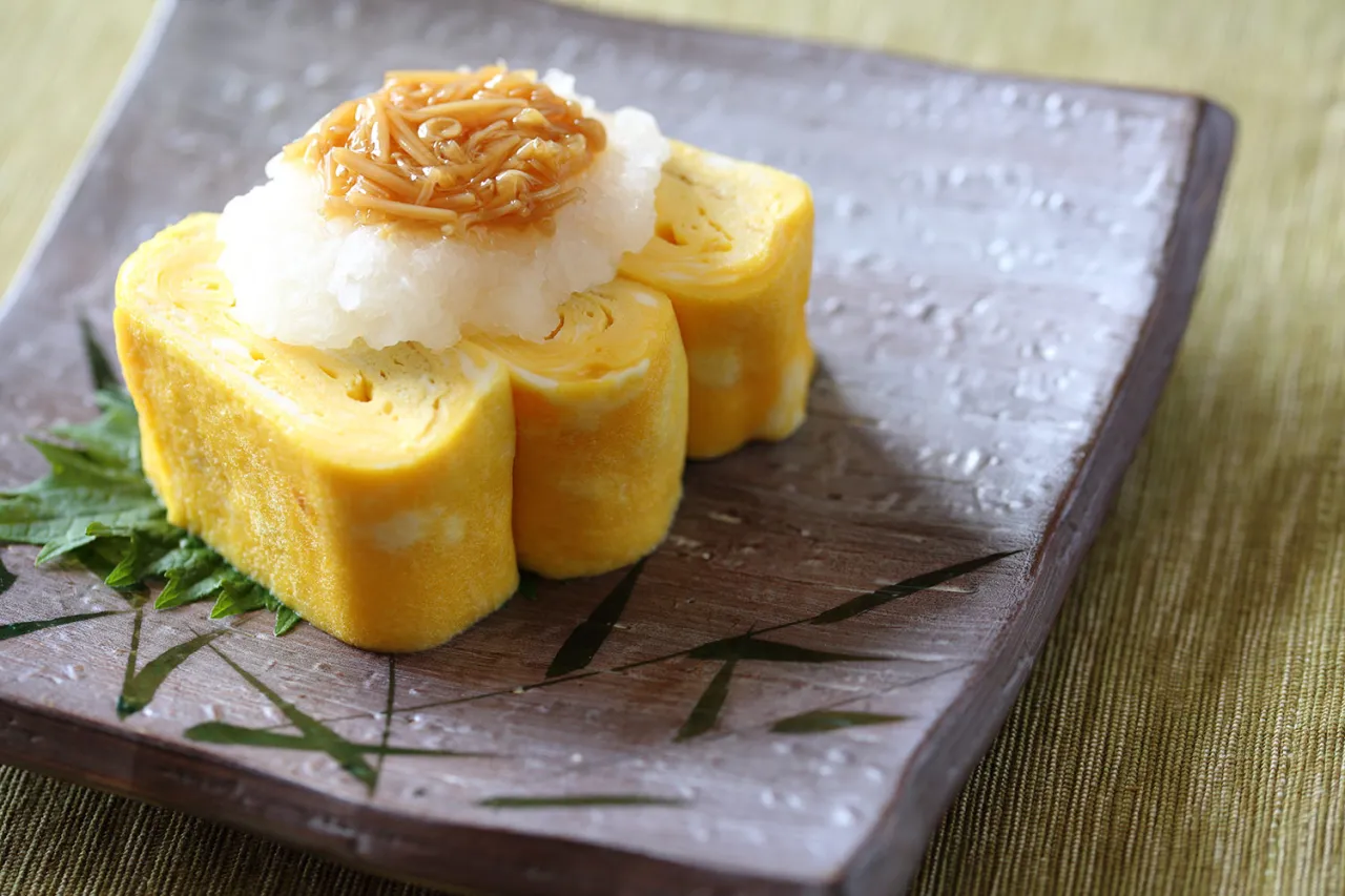 Tamago przepis: zwinięte omlety jajeczne z tartą rzodkiewką i grzybami enoki na talerzu.