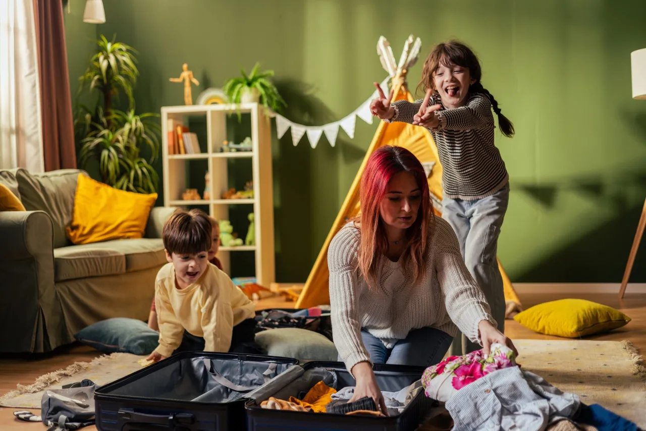 Rodzina z dzieckiem pakująca walizkę, obok leżą zabawki i ubranka dziecięce