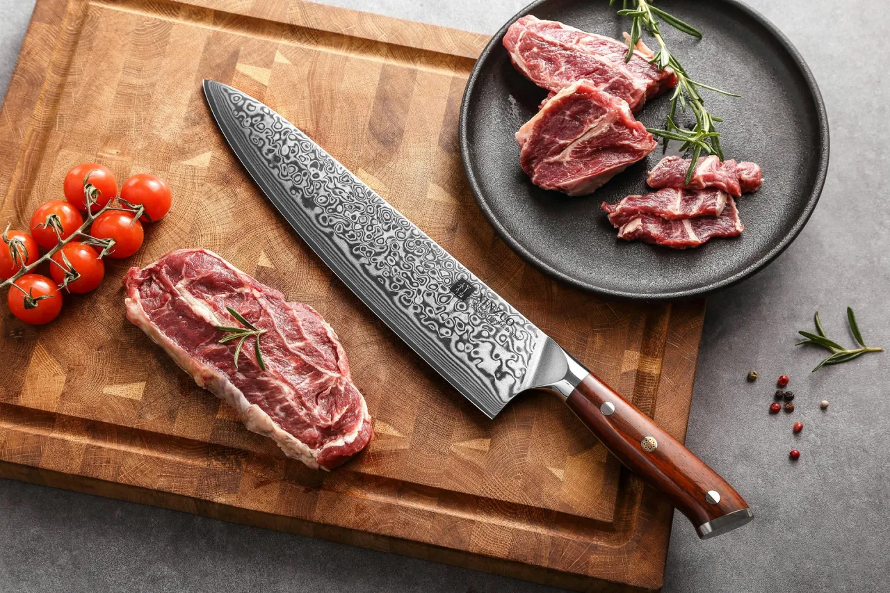 Ostrze noża z wzorem damasceńskim obok surowej wołowiny i pomidorków. Idealne narzędzie, by dowiedzieć się, jak kroić wołowinę w paski.