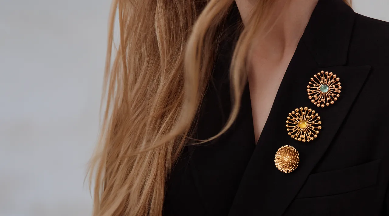 Elegancko jak nosić broszki: trzy złote ozdoby w kształcie kwiat&oacute;w na czarnej marynarce.