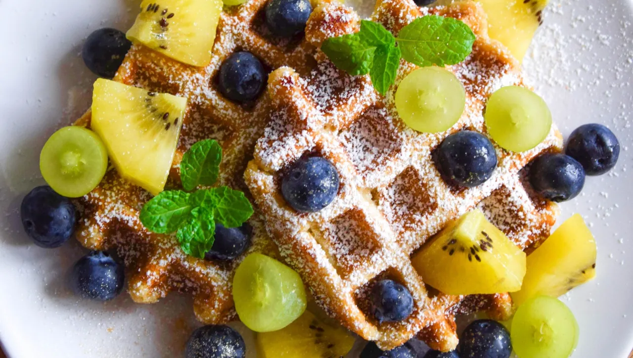 Pyszny przepis na zdrowe gofry z owocami: kiwi, borówkami i winogronami, posypane cukrem pudrem.