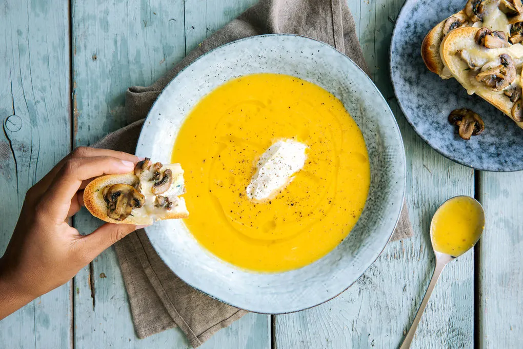 cremige K&uuml;rbissuppe in einer Schale mit K&uuml;rbiskernen und einem L&ouml;ffel serviert