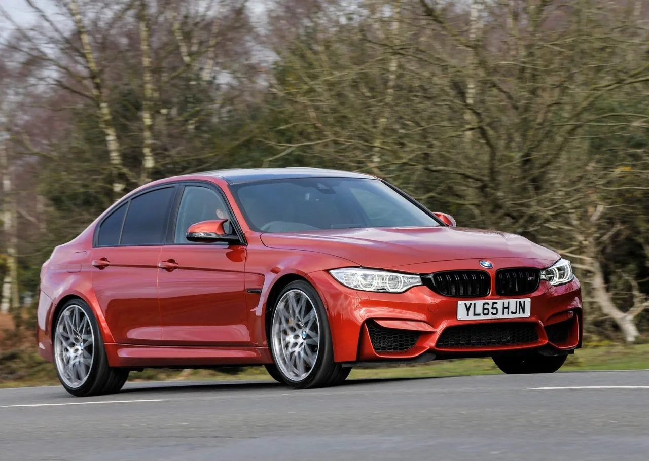 Pomarańczowe BMW M3 F80 pędzi po drodze, otoczone drzewami.