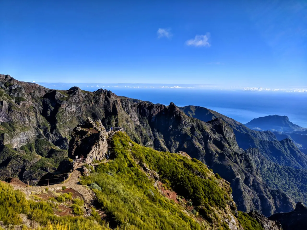 Widok na jedne z najpiękniejszych szlaków trekkingowych na Maderze: lewady i szczyty. Kamienna ścieżka wije się pośród zielonych zboczy, prowadząc w stronę skalistych gór.