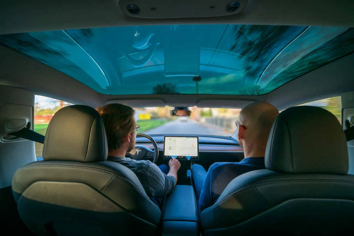Dw&oacute;ch mężczyzn w Tesli z panoramicznym dachem. Zastanawiasz się, ile kosztuje najtańsza Tesla?
