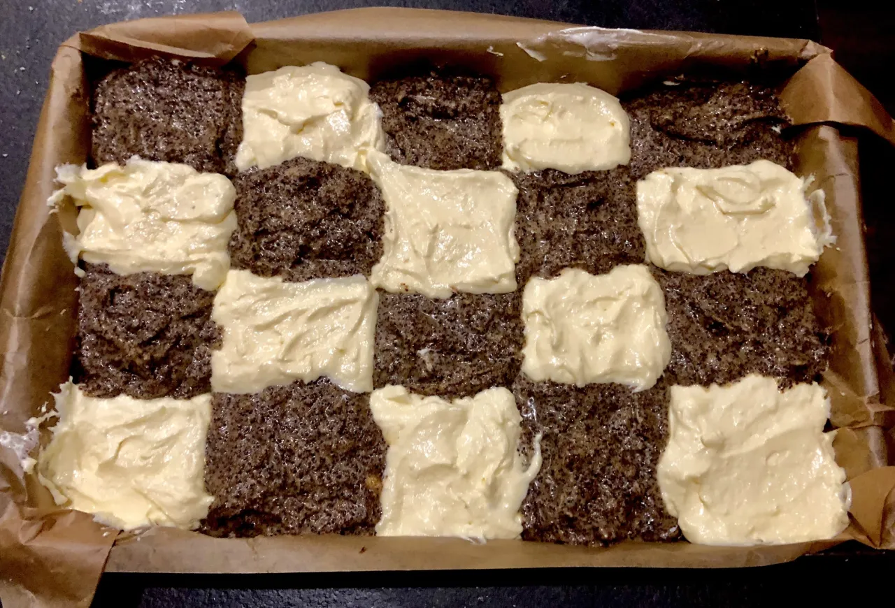 Przygotowania do pieczenia ciasta z serem i makiem. Warstwy ciasta makowego przeplatane kremem serowym w blasze wyłożonej papierem.