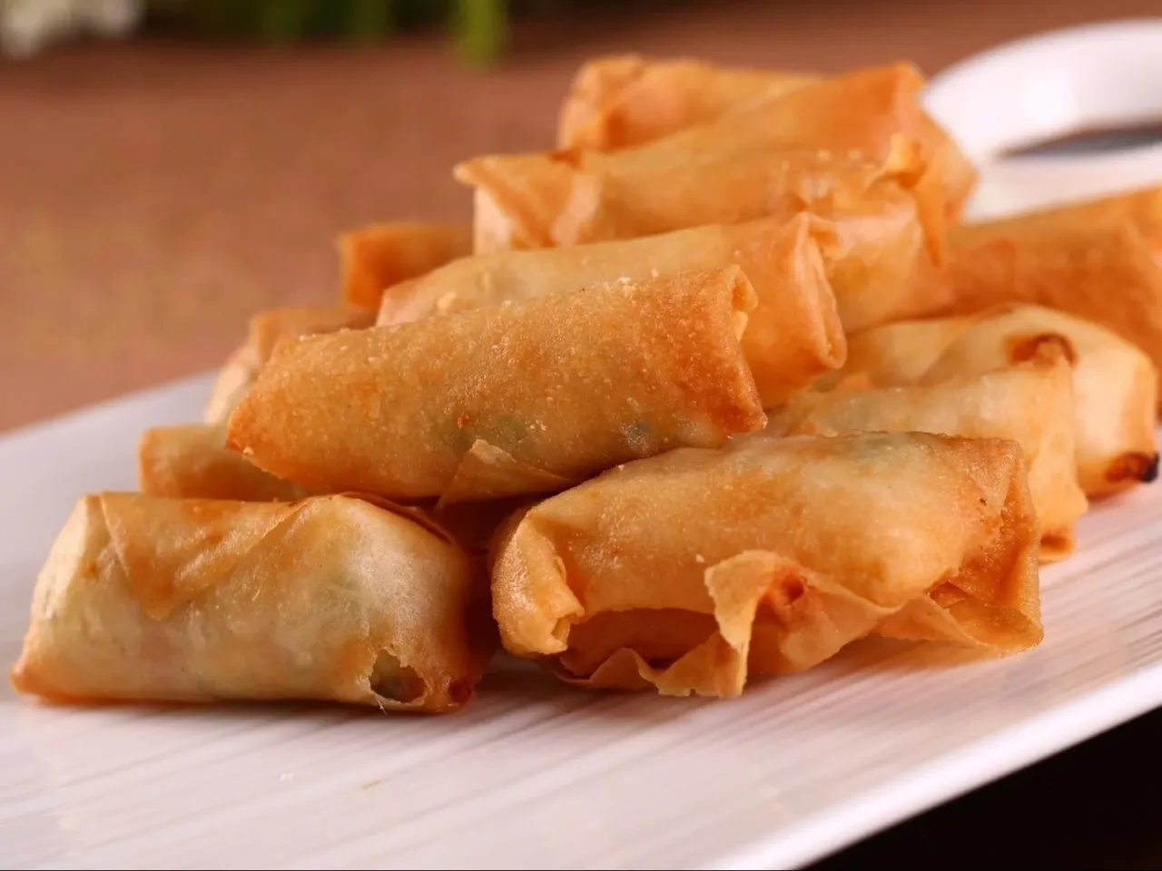Chrupiące spring rolls ułożone na białym talerzu, gotowe do zanurzenia w sosie.