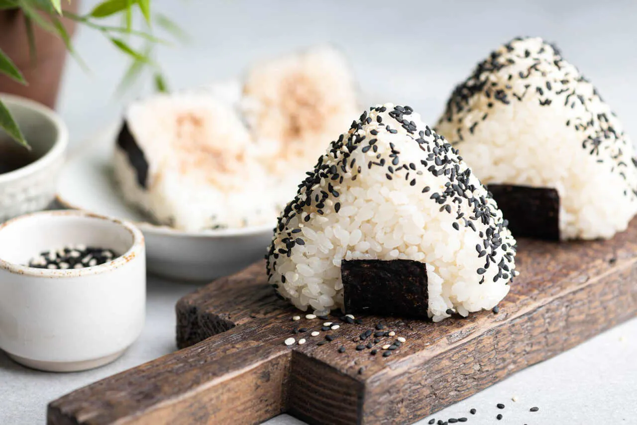 Tr&oacute;jkątne onigiri sushi z czarnym sezamem i kawałkiem nori na drewnianej desce.