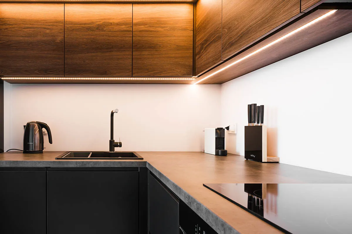 Nowoczesna kuchnia z drewnianymi frontami szafek i dyskretną listwą oświetleniową led, która tworzy ciepłą atmosferę.