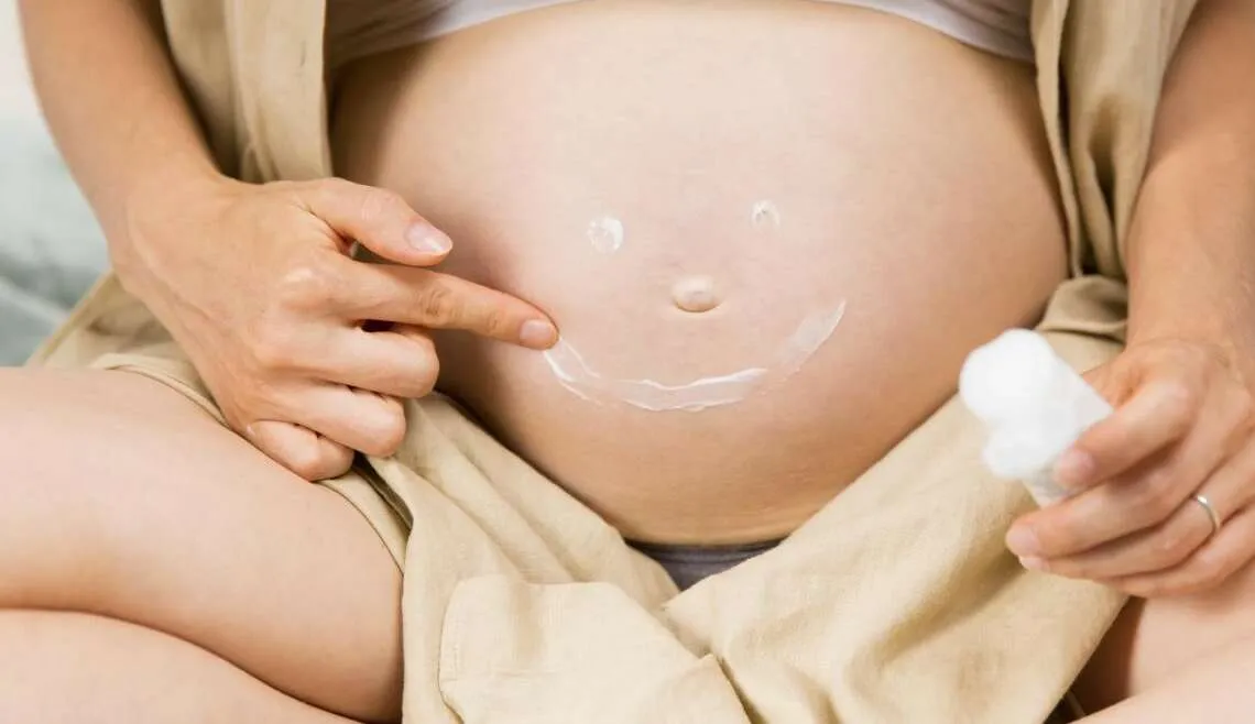 Kobieta w ciąży smarująca brzuch olejkiem na rozstępy