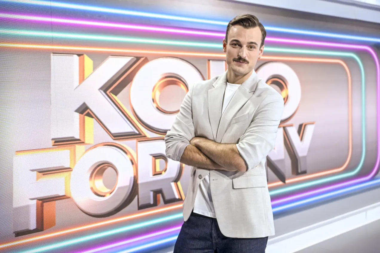 Mężczyzna w jasnej marynarce stoi przed logo 